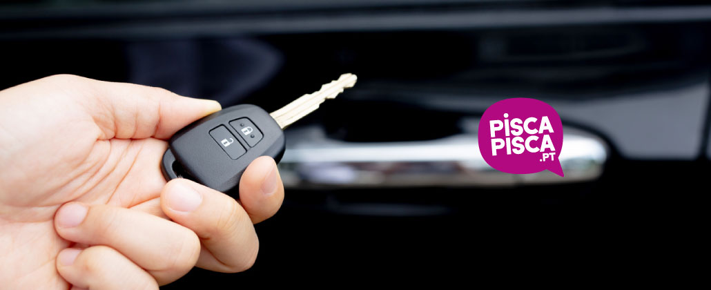 mão humana segura a chave de um carro. Ao fundo, vê-se o puxador de uma porta do carro